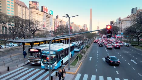 Low-level-aerial-drone-flyover-across-multiple-lanes-of-motorway-and-busway-capturing-buzzing-downtown-cityscape-with-heavy-traffics-on-9-de-Julio-avenue-at-rush-hours,-Buenos-Aires-city,-Argentina