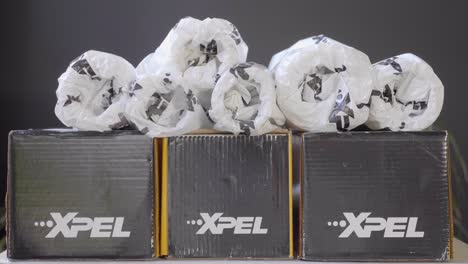 Xpel-Car-Wrap-Foil-Rolls-Wrapped-in-Paper-Stacked-on-Cardboard-Boxes