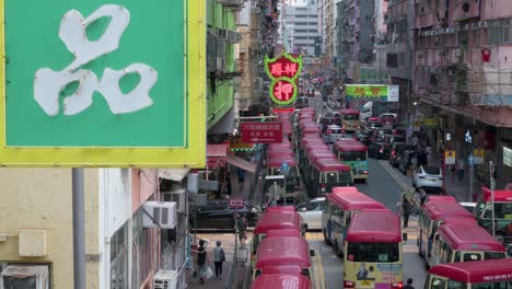 A-neon-sign-is-seen-in-the-foreground-as-Chinese-pedestrians,-commuters,-and-buses-are-stationed-on-a-hectic-street-in-Mong-Kok-district,-Hong-Kong