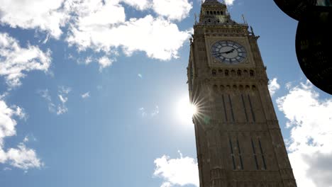 Looking-Up-At-Big-Ben-Clock-Tower-With-Star-Shaped-Sun-Peaking-Behind-On-Sunny-Day