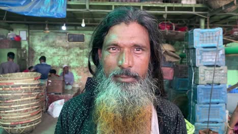 Closeup-portrait-of-bearded-vendor-man-worker-standing-in-front-of-camera-in-a-market,-dolly-out