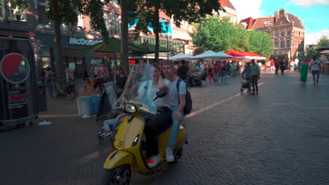 Goofy-and-happy-scooter-riders-giving-the-finger-to-the-cameraman-while-riding-through-centrum