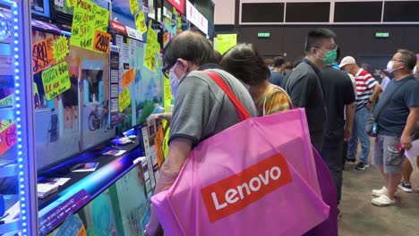 Ein-Chinesischer-Käufer-Hält-Eine-Lenovo-einkaufstasche-In-Der-Hand,-Während-Er-Nach-Fernsehgeräten-Sucht,-Die-Auf-Dem-Computer--Und-Kommunikationsfestival-In-Hong-Kong-Ausgestellt-Werden,-Während-Leute-Ermäßigte-Elektronische-Produkte-Kaufen