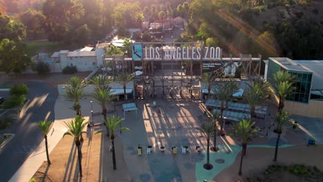 Aerial-View-of-Los-Angeles-Zoo,-California-USA,-Rising-Above-Sign-and-Entrance-Gates-With-Sunset-Sunlight-as-Backlight,-Drone-Shot