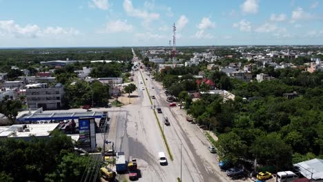 A-bright-sunny-day-as-cars-drive-through-Tulum-Mexico-on-a-long-highway-road,-aerial