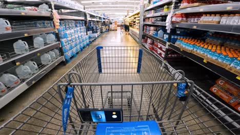 POV-while-pushing-a-cart-through-Walmart-past-shelves-of-water-and-past-refrigerated-shelves