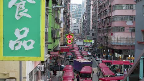 An-urban-Hong-Kong-scene-shows-a-neon-sign-in-the-foreground-as-Chinese-pedestrians,-commuters,-and-buses-are-stationed-on-a-hectic-street-in-Mong-Kok-district