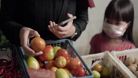 Tomatenkäufer-Pflückt-Frische-Tomaten-Auf-Einem-Traditionellen-Indonesischen-Markt-Mit-Einem-Mädchen-Im-Hintergrund,-Das-Es-Betrachtet