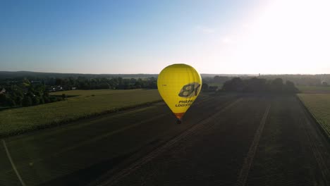 Aerial-Morning-Sunrise-View-Of-Bright-Yellow-Hot-Air-Balloon-Flying-Over-Rural-Field-In-The-Netherlands