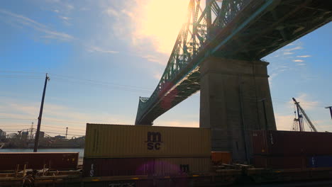 Freight-Train-Under-Jacques-Cartier-Steel-Bridge-Montreal-City-Canada,-Urban-Rigid-Metallic-Elevated-Structure-for-Transportation,-Tilt-Up-View-of-Architectural-Infrastructure-and-Engineering