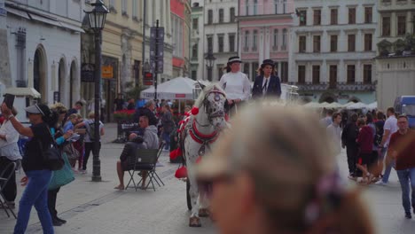 On-a-Kraków,-Poland-street-where-many-people-are-walking,-two-women-are-driving-a-horse-drawn-carriage-which-is-pulled-by-two-white-horses