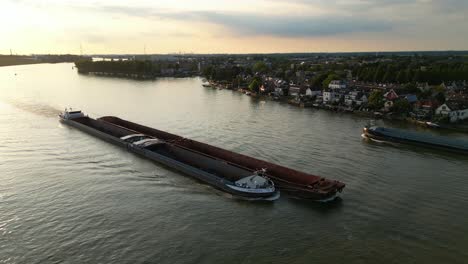 Aerial-View-Over-Amoureus-Push-Freighter-Sailing-Along-Beneden-Merwede-During-Sunset-Passing-Another-Ship