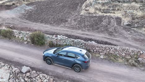 Aerial-drone-shot-of-a-moving-mazda-car-over-a-rocky-highway-in-the-mountains-of-peru-south-america