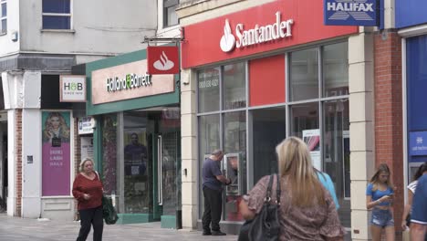 Tiendas-Y-Banco-Santander-Con-Compradores-Caminando-Y-Cajero-Automático-En-Uso