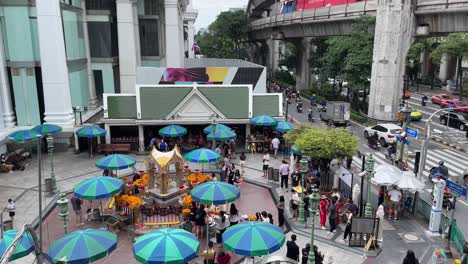 A-panning-view-of-the-moving-BTS-Sky-train-with-traffic-flow-to-the-famous-Erawan-Shrine-at-the-Ratchaprasong-intersection-on-Ratchadamri-Road-in-Bangkok,-Thailand