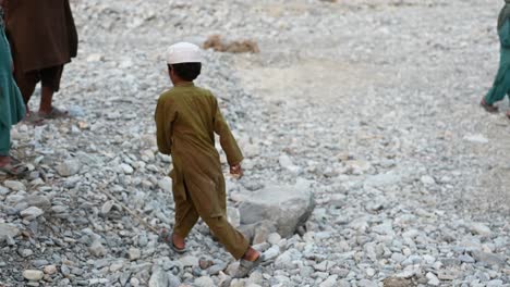 Back-view-of-the-small-child-walking-in-pebble-filled-land-of-the-Balochistan,-Pakistan