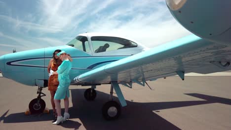 Two-Female-Models-Posing-Next-To-Classic-Vintage-Teal-Colored-Airplane