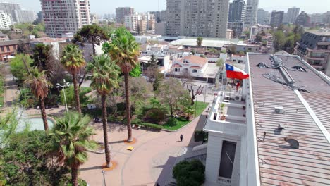 Aerial-view-dolly-in-of-the-Ñuñoa-municipality-with-the-Chilean-flag-on-the-top-of-the-roof-and-people-walking-on-a-sunny-day