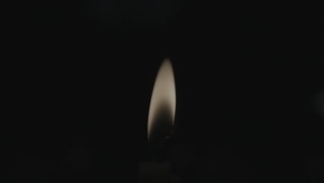 A-closeup-shot-of-a-glowing-candle-flame-slowly-swaying,-surrounded-by-darkness
