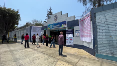 Tilt-down-shot-of-Peruvian-voters-peacefully-entering-polling-station-during-municipal-elections-on-calm-sunny-day-at-La-Molina,-Lima,-Peru