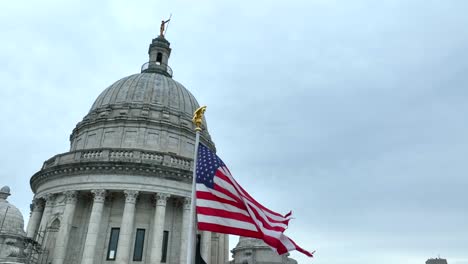American-flag-waves-in-front-of-dome-of-state-Capitol-building-in-Providence,-Rhode-Island