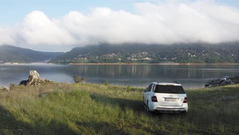 Scenic-aerial-view-of-white-Mercedes-off-road-car-parked-on-shores-of-Mavrovo-lake-in-Macedonia