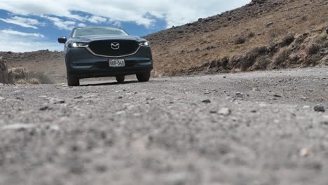 Toma-Estática-De-Un-Auto-Mazda-Parado-En-Un-Camino-Rocoso-En-Perú-En-Las-Montañas-Con-Un-Viento-De-Polvo-Y-Vista-Del-Cielo
