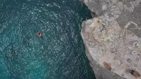 Rising-overhead-slo-mo-aerial-as-man-cliff-jumps-with-a-twist-into-sea