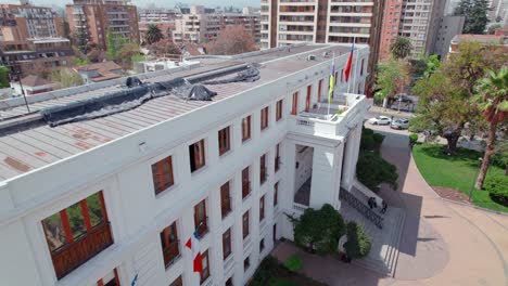 Vista-Aérea-Del-Edificio-Del-Municipio-De-Ñuñoa,-Chile-Con-La-Bandera-Al-Frente,-Día-Soleado