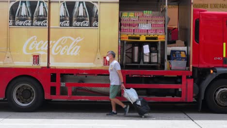 A-man-walks-past-a-Coca-Cola-delivery-truck-as-soft-drink-brand-company-goods-are-being-offloaded-to-restaurants-and-other-clients-nearby