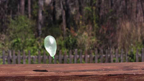A-green-water-balloon-bounces-on-a-wooden-bench-four-times