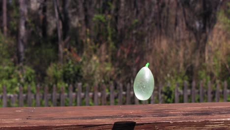 A-Green-Water-Balloon-drops-onto-a-wooden-bench-and-bounces-off