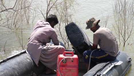 Dos-Hombres-Revisando-El-Motor-Del-Bote-Inflable-En-Sindh,-Pakistán