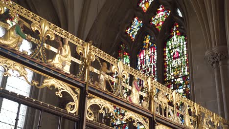 Wells-Cathedral-Architecture,-Goldstreifen-Mit-Figuren-Von-Betenden-Menschen,-Buntglasfenster-Im-Hintergrund
