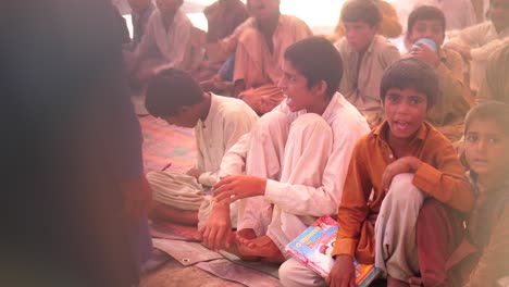 Video-Der-Großen-Gruppen-Von-Jungen,-Die-Mit-Büchern-In-Der-Hand-In-Der-Schule-Im-Ländlichen-Pakistan-Auf-Der-Matte-Im-Boden-Sitzen
