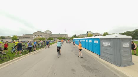 Crowd-of-cyclists-and-Bike-the-Drive-2022-participants-arrive-at-the-Museum-of-Science-and-Industry-rest-stop-in-Chicago,-IL---old-neoclassical-building-in-the-background-people-walking-their-bikes