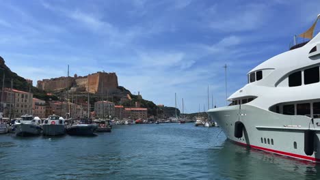 Große-Luxuriöse-Und-Teure-Yacht,-Die-Im-Hafen-Von-Bonifacio-Mit-Schloss-Und-Zitadelle-Auf-Einer-Klippe-Festgemacht-Ist