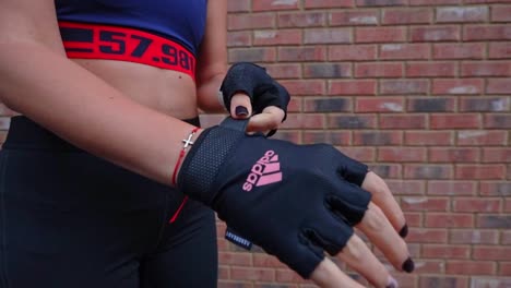 Close-up-on-young-athletic-female-placing-hands-into-branded-sports-workout-adidas-gloves