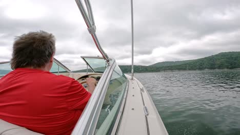 The-back-of-man-in-red-shirt-driving-a-sports-boat-cruising-on-Table-Rock-Lake-in-Ozark-Mountains-in-Missouri-USA-on-a-cloudy-day