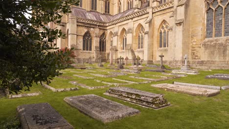 Wells-Cathedral-outside-cemetery,-camera-rotating-to-the-right-showing-some-of-the-graves-and-the-grave-stones-and-crosses-with-the-cathedral-facade-in-the-background