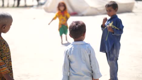 Three-small-boys-standing-outside-in-the-sunny-day-and-small-girl-running-in-the-background-in-Pakistan