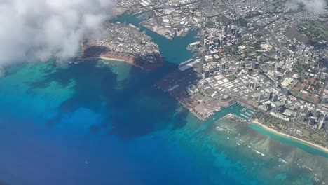 Airplane-view-flying-over-Honolulu's-busy-downtown-skyline-overlooking-the-crystal-clear-blue-waters-of-Oahu,-Hawaii-