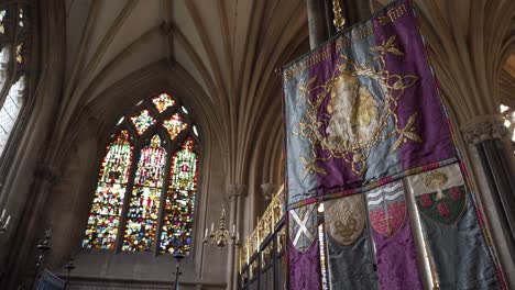 Wells-Cathedral-ceiling-arches-and-stained-glass-windows,-ornate-flag,-camera-rotating-to-the-left