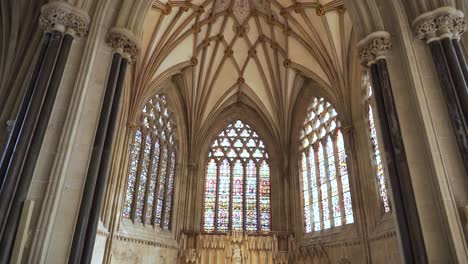 Wells-Cathedral-ceiling-arches,-camera-moving-down-from-the-ceiling-showing-the-tainted-glass-windows-and-the-columns