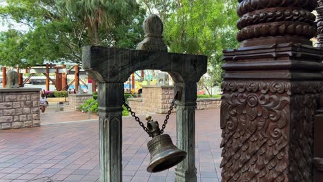 Handgeführte-Aufnahme,-Die-Geschnitzte-Holzdetails-Eines-Dreistöckigen-Hohen-Denkmalgeschützten-Gebäudes-Einfängt-Nepalesische-Pagode-Mit-Einer-Bronzenen-Glocke,-Die-Vor-Dem-Haupteingang-Läutet-Und-Schwingt,-Parklands,-South-Bank-Brisbane-City