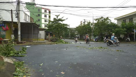 Tropical-Storm-Aftermath,-Trees-and-Leaves-on-City-Street-Streets-and-Motorbike-Riders-Passing-By