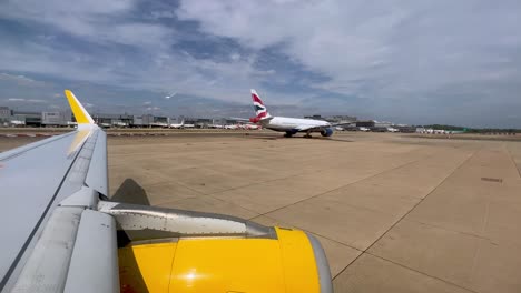 View-of-yellow-airplane-wing-and-engine-moving-on-ground-in-London-Gatwick-British-airport-in-England