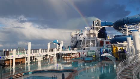 NCL,-Norwegian-Bliss-cruise-ship-pool-deck-after-rain-showing-smokestack-and-rainbow