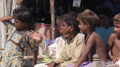 Video-of-the-small-poor-boys-and-girl-sitting-in-the-khatiya-or-bed-placed-outside-in-the-sun-and-looking-at-side-and-laughing-in-Maher,-Sindh