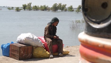 Video-of-the-teenage-boys-sitting-on-the-sack-of-supplies-and-looking-at-the-lake-flowing-behind-him-in-Maher,-Sindh